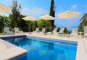 A swimming pool with lounge chairs and umbrellas, surrounded by a fence and trees. - Apartments Villa Lukas (Konavle)