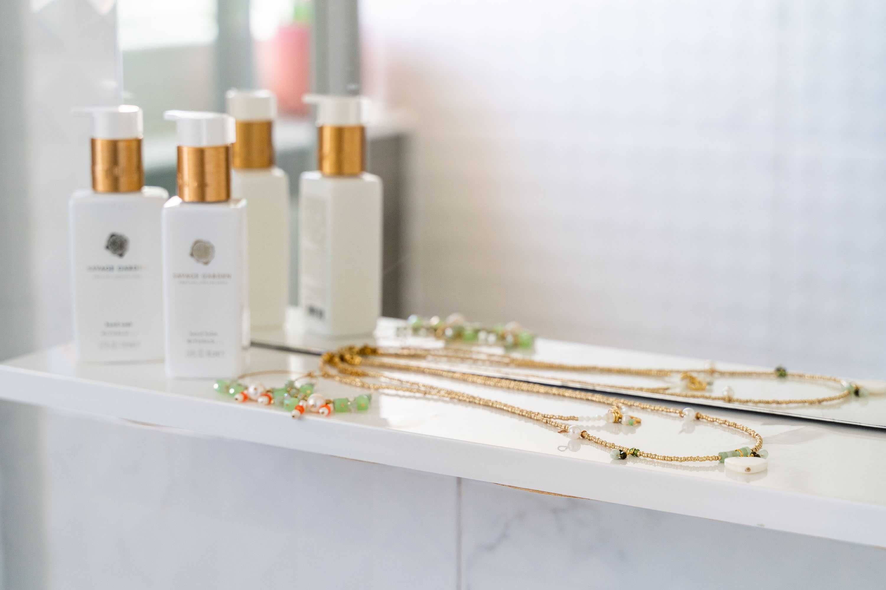 A display of skincare products and jewelry on a white marble counter.