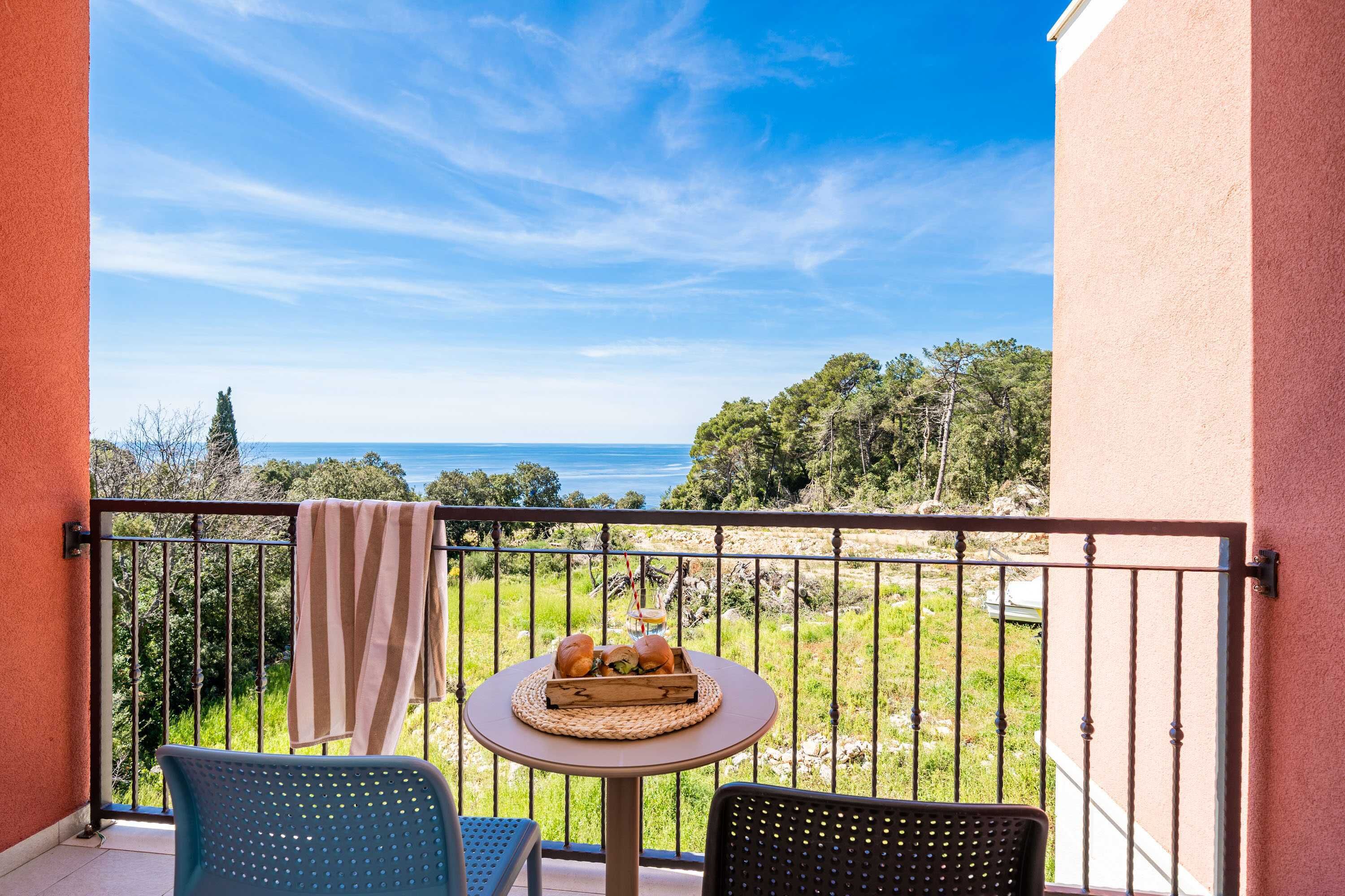 A balcony with a table set for two, overlooking a grassy area and the sea.