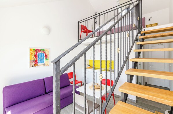 A modern living space with a purple sofa, a dining table with red chairs, and a staircase with wooden steps and metal railings. - Apartments Villa Lukas (Konavle)