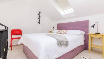A bedroom with a bed, a red chair, a bedside table, and a skylight.