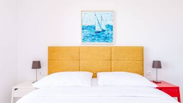 Una camera d'albergo con un letto, una testiera, due comodini e un quadro con dei velieri sulla parete.