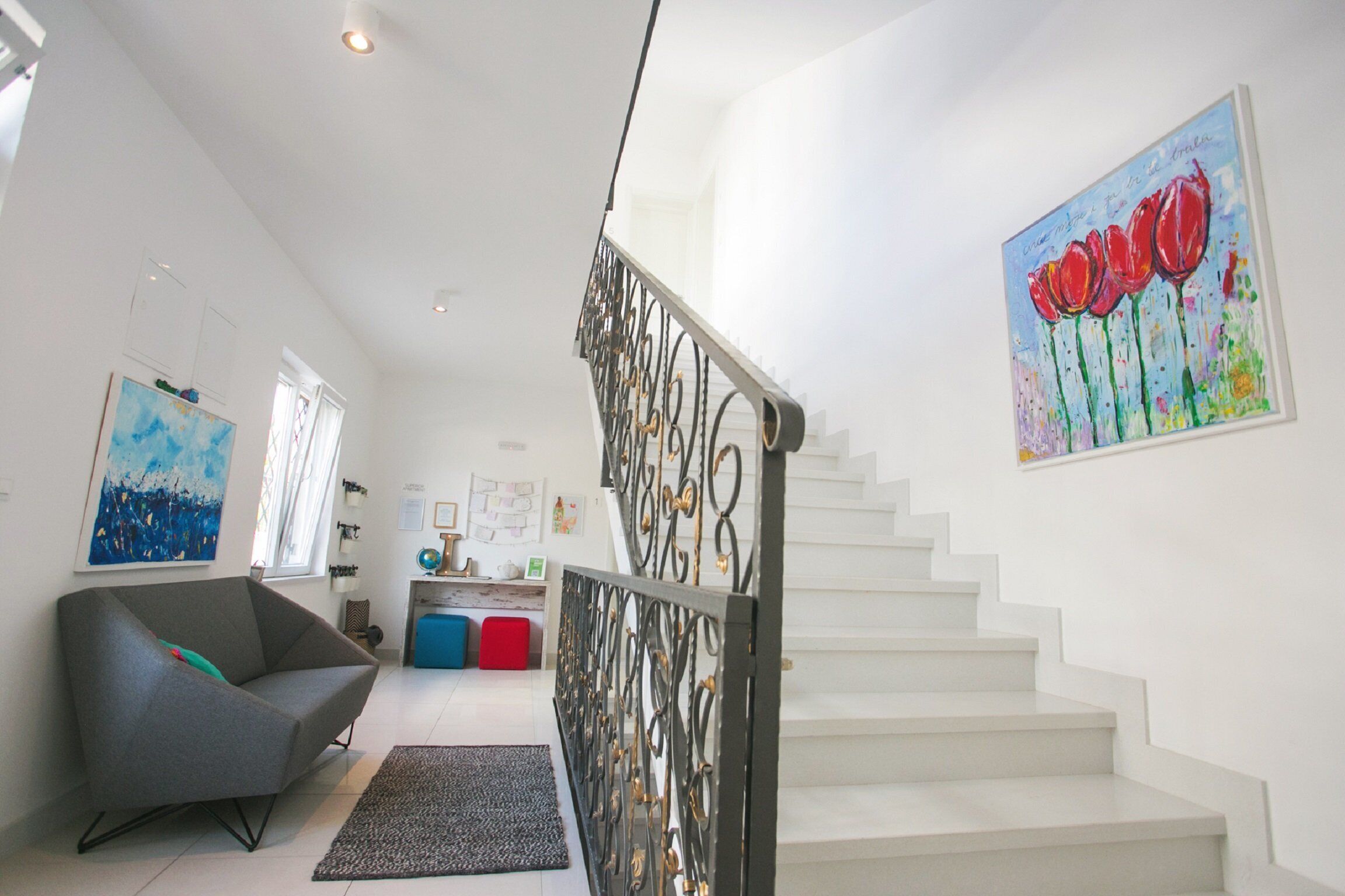 Ein modernes Interieur mit einer Treppe, einem grauen Sessel und einem farbenfrohen Gemälde an der Wand.