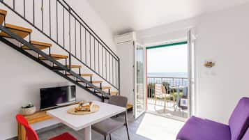 A modern apartment with a staircase, a dining area, a living room with a purple sofa, and a balcony with a view.