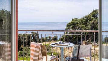 A balcony with a table and chairs, overlooking a coastal landscape with trees and the sea.