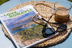 A magazine titled "in LOVE with Konavle," a pair of glasses, and a cup of coffee on a woven mat. - Apartments Villa Lukas (Konavle)