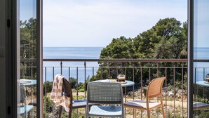 Een balkon met een tafel en stoelen, met uitzicht op een prachtig zee- en boslandschap.