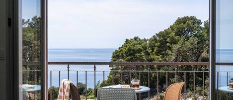 A balcony with a table and chairs, overlooking a scenic view of the sea and trees.