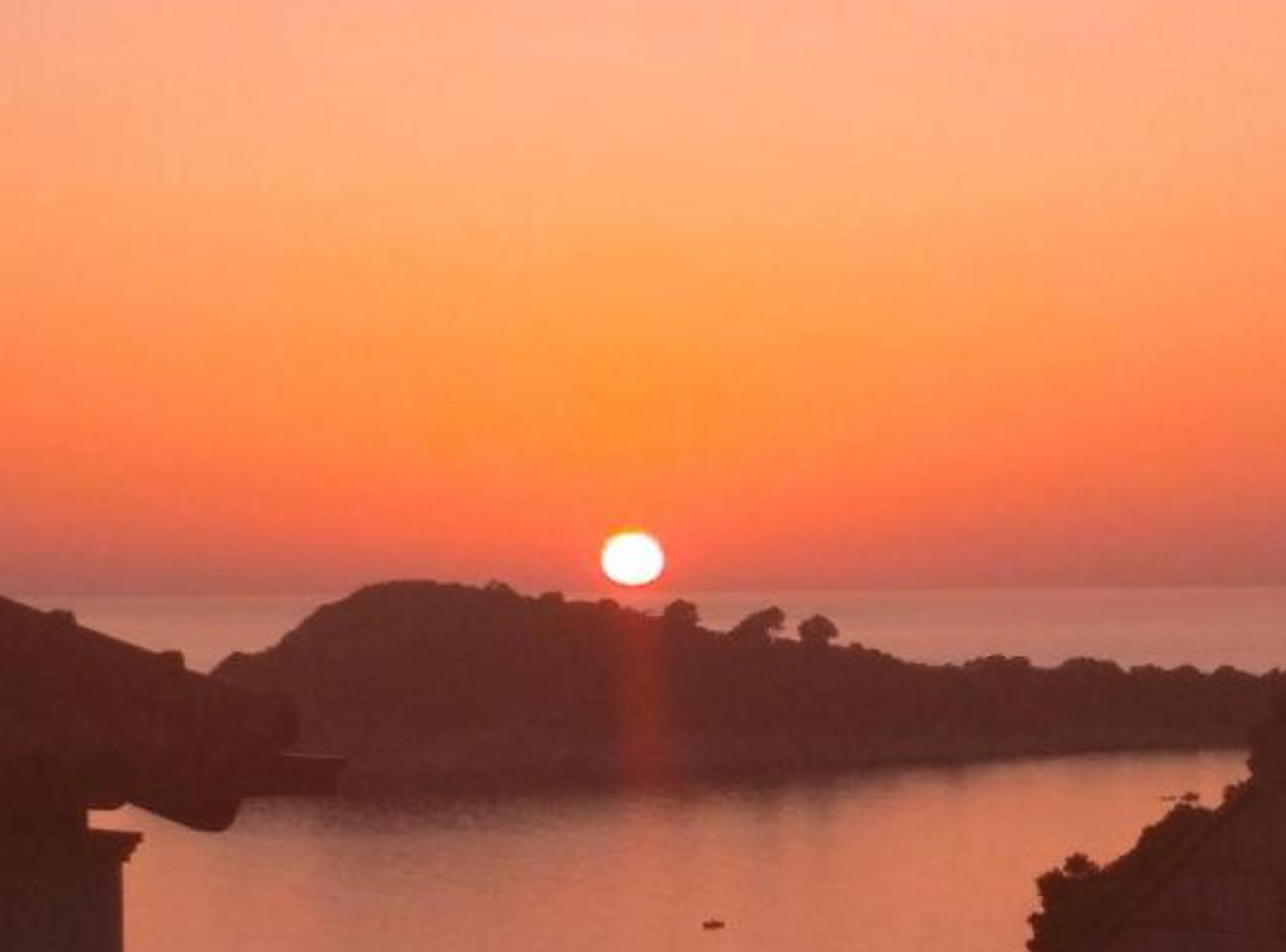 A sunset over a calm body of water with silhouetted landforms in the foreground.