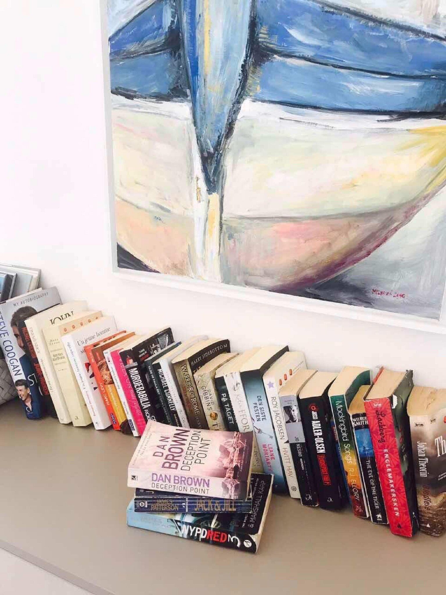 A bookshelf with various books and a painting above it.