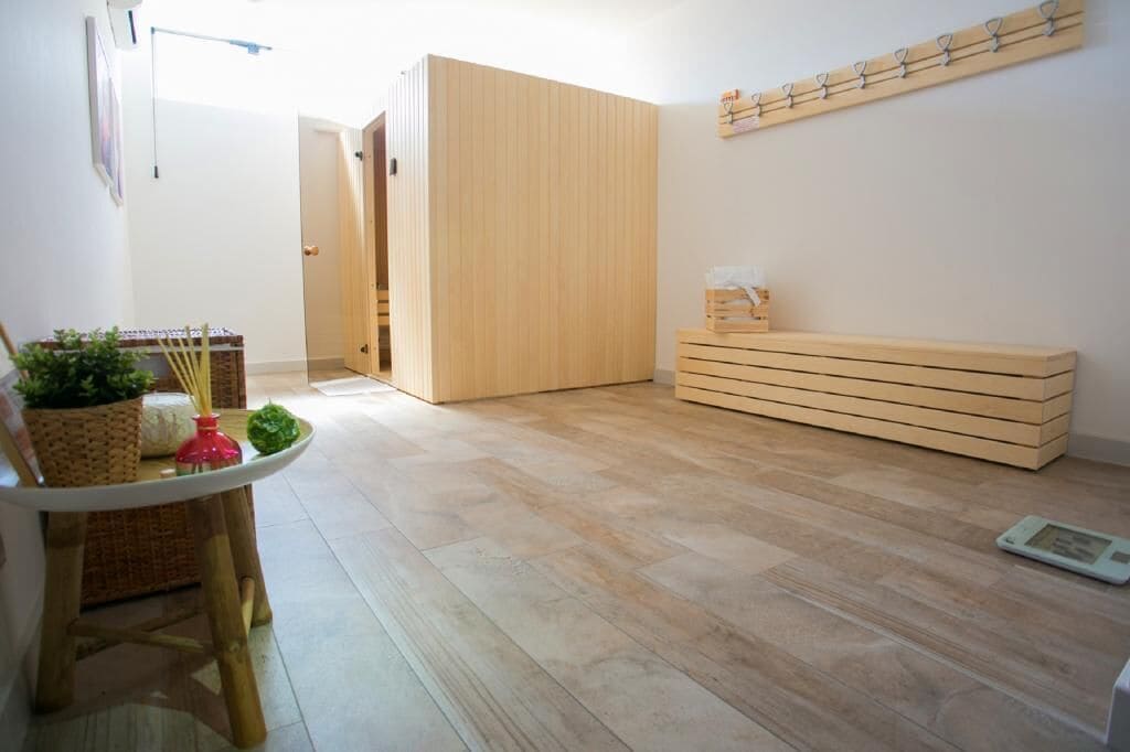Habitació amb terra de fusta, una taula petita amb una cistella i una planta, una banca de fusta i un penjador de parets.