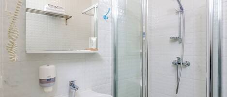 A bathroom with a glass-enclosed shower, a white sink, a soap dispenser, and a towel rack.