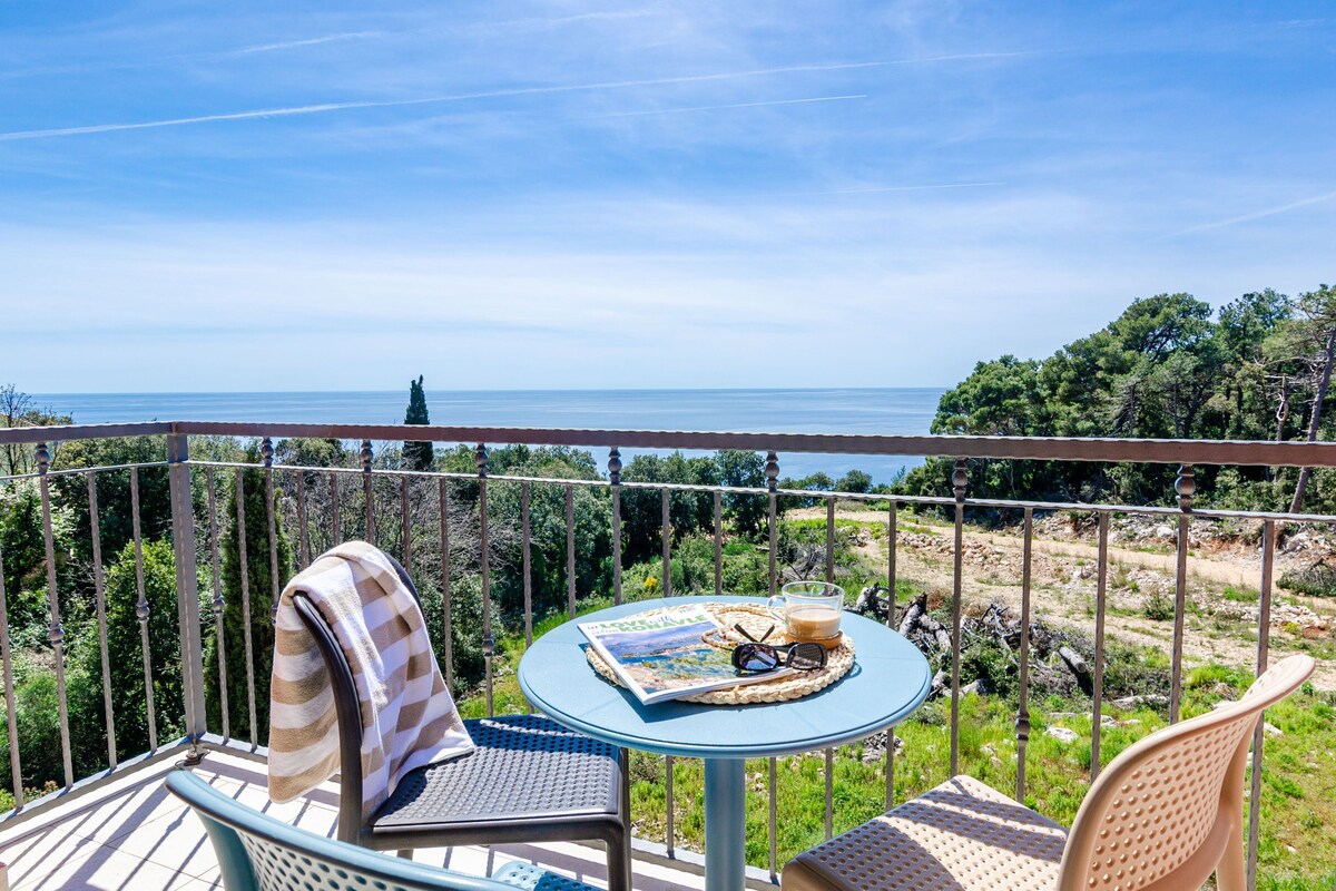 A balcony with a round table, chairs, and a view of the sea.