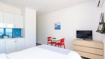 Moderni hotellihuone, jossa on sänky, työpöytä ja kaksi punaista tuolia, televisio puisen lipaston päällä sekä pieni taulu seinällä.