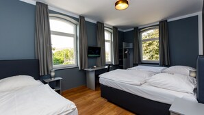 Ein modernes Hotelzimmer mit zwei Betten, einem Schreibtisch, einem Fernseher und großen Fenstern mit Vorhängen.