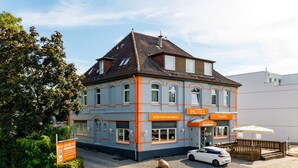 Ein Hotel mit moderner Fassade, ein geparktes Auto davor und eine Schilderung der Hotelservices.