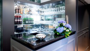 Un espace bar doté d’une vitrine où sont exposées des bouteilles et des verres, d’un vase décoratif contenant des fleurs et d’un luminaire moderne.