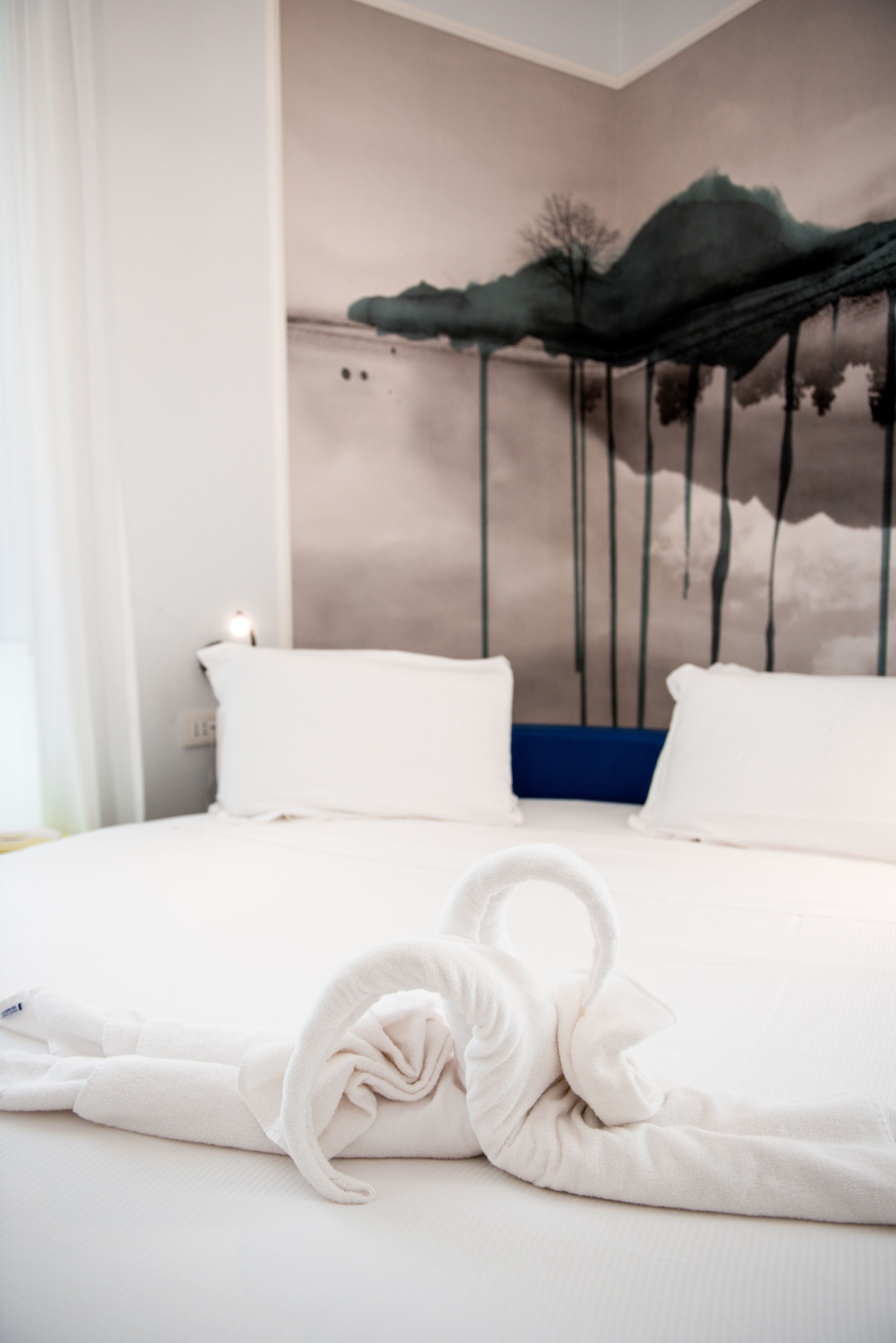 A hotel room with a bed, white pillows, a towel, and a wall mural.