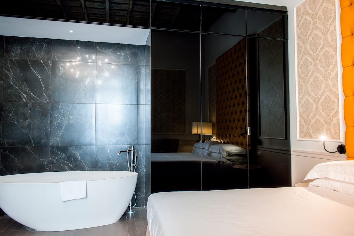 Ein modernes Badezimmer mit einer freistehenden Badewanne, einem großen Spiegel und einem Bett mit weißer Bettwäsche.