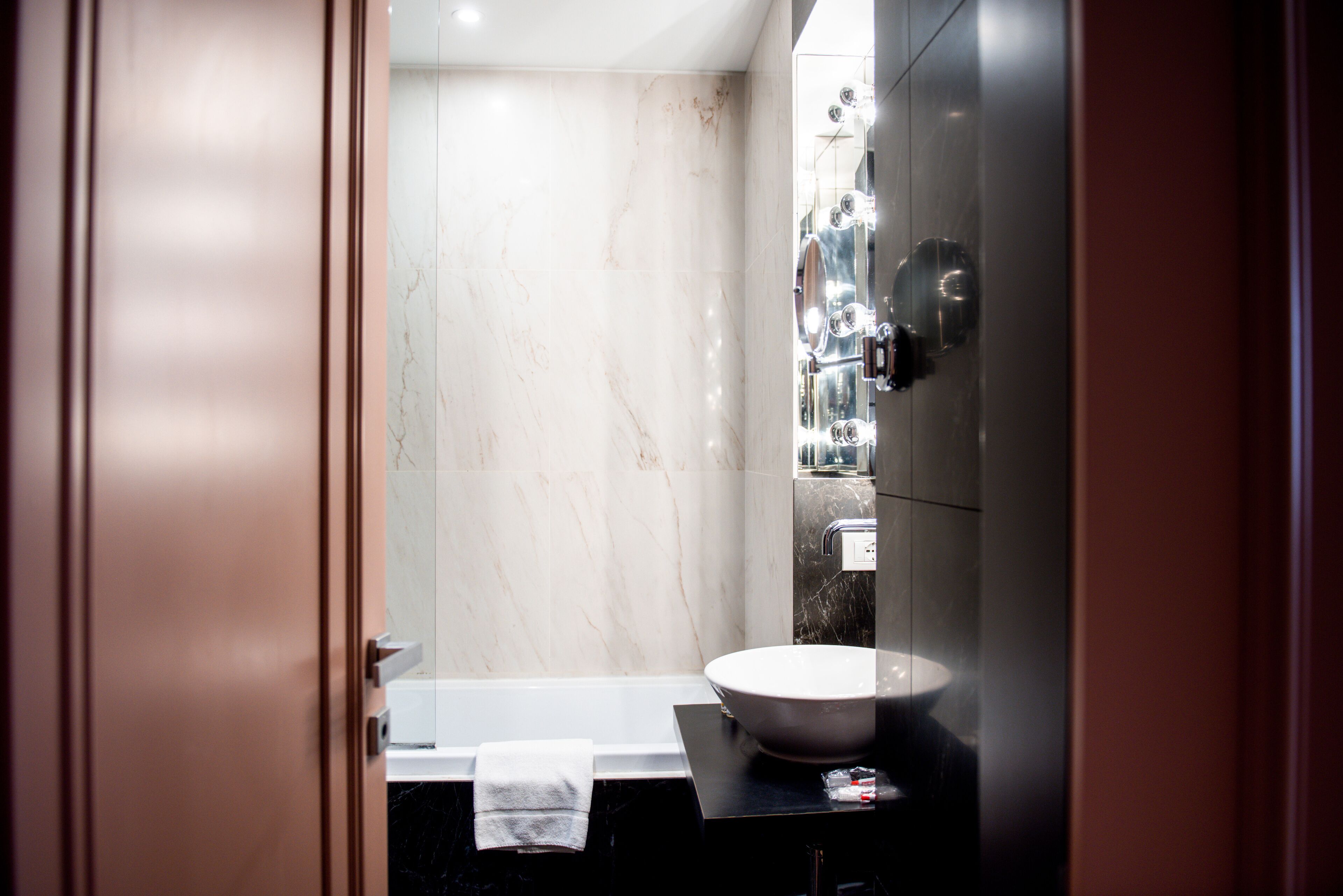 A modern bathroom with a marble wall, a white sink, and a bathtub.