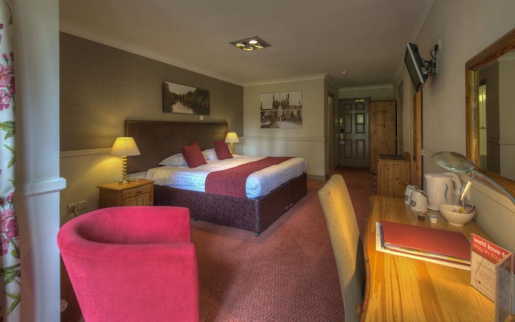 Een hotelkamer met een bed, nachtlampjes, een bureau met een spiegel en een stoel.