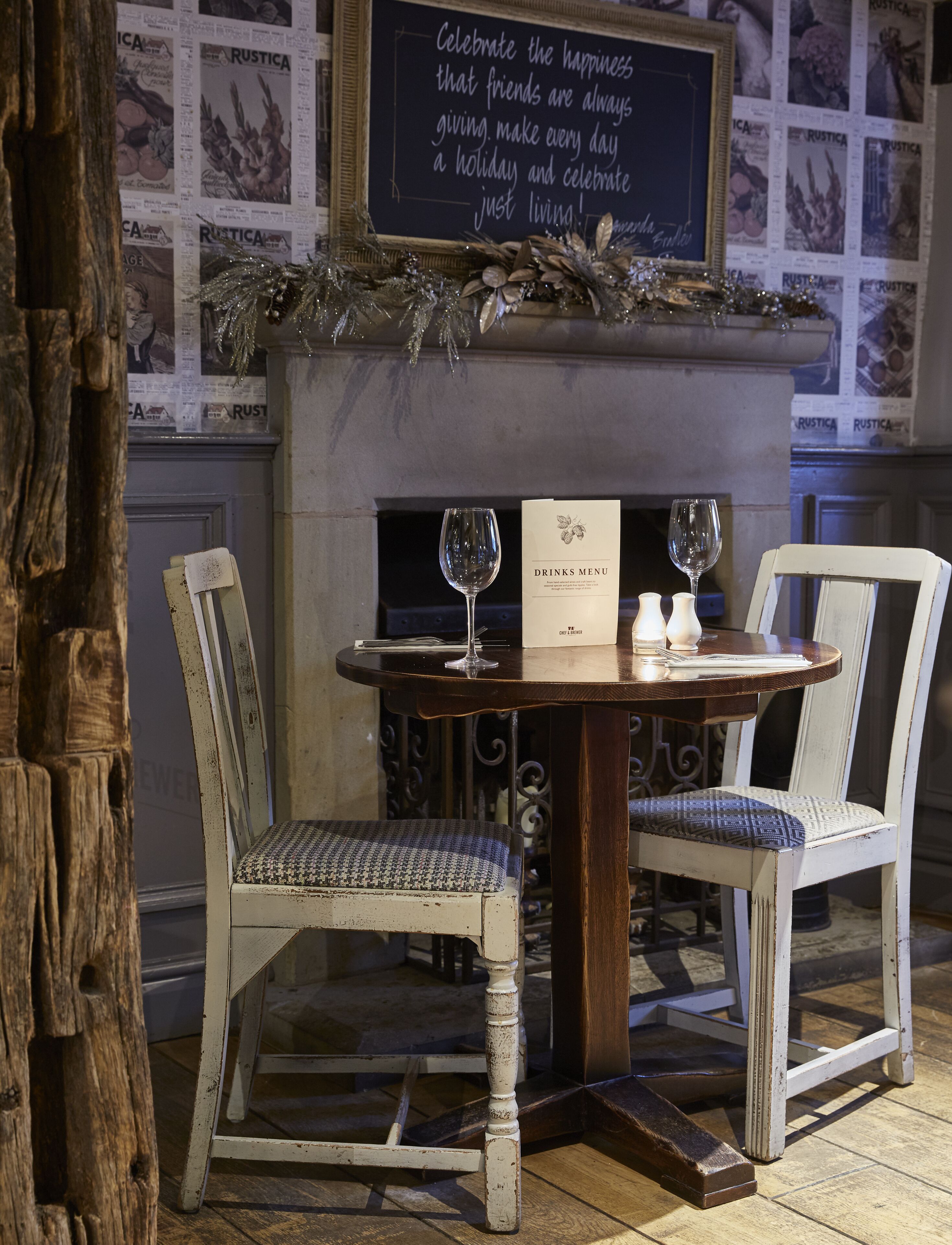 A rustic dining area with a wooden table, two chairs, a menu, and a decorative wall with a chalkboard sign.