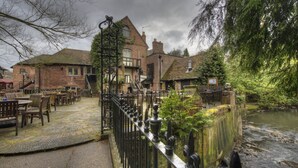 A riverside pub with outdoor seating, brick buildings, and a stone pathway. - The Old Mill by Chef and Brewer Collection (Coventry)