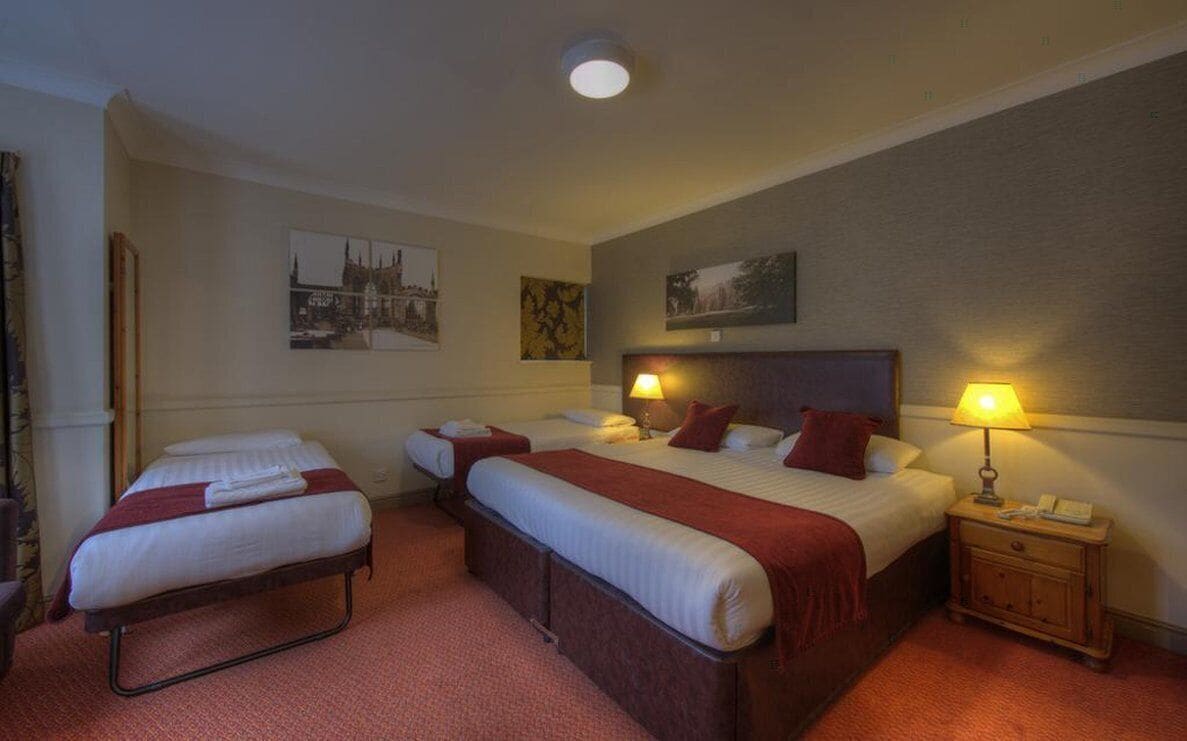 A hotel room with two single beds, a double bed, and a small bedside table with a lamp.