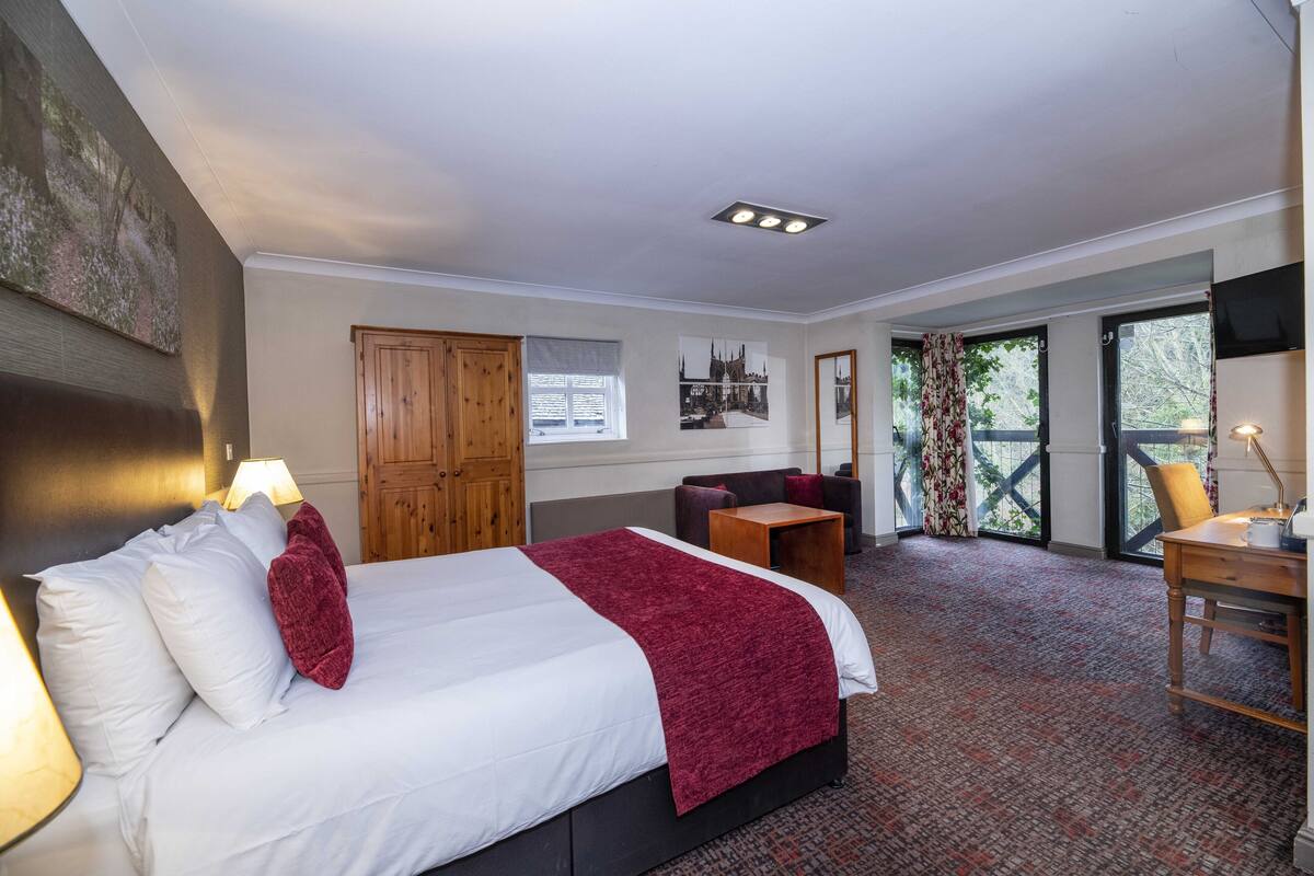 Ein Hotelzimmer mit einem großen Bett, einem Schreibtisch, einem Sessel, einer Couch und einem Fernseher.