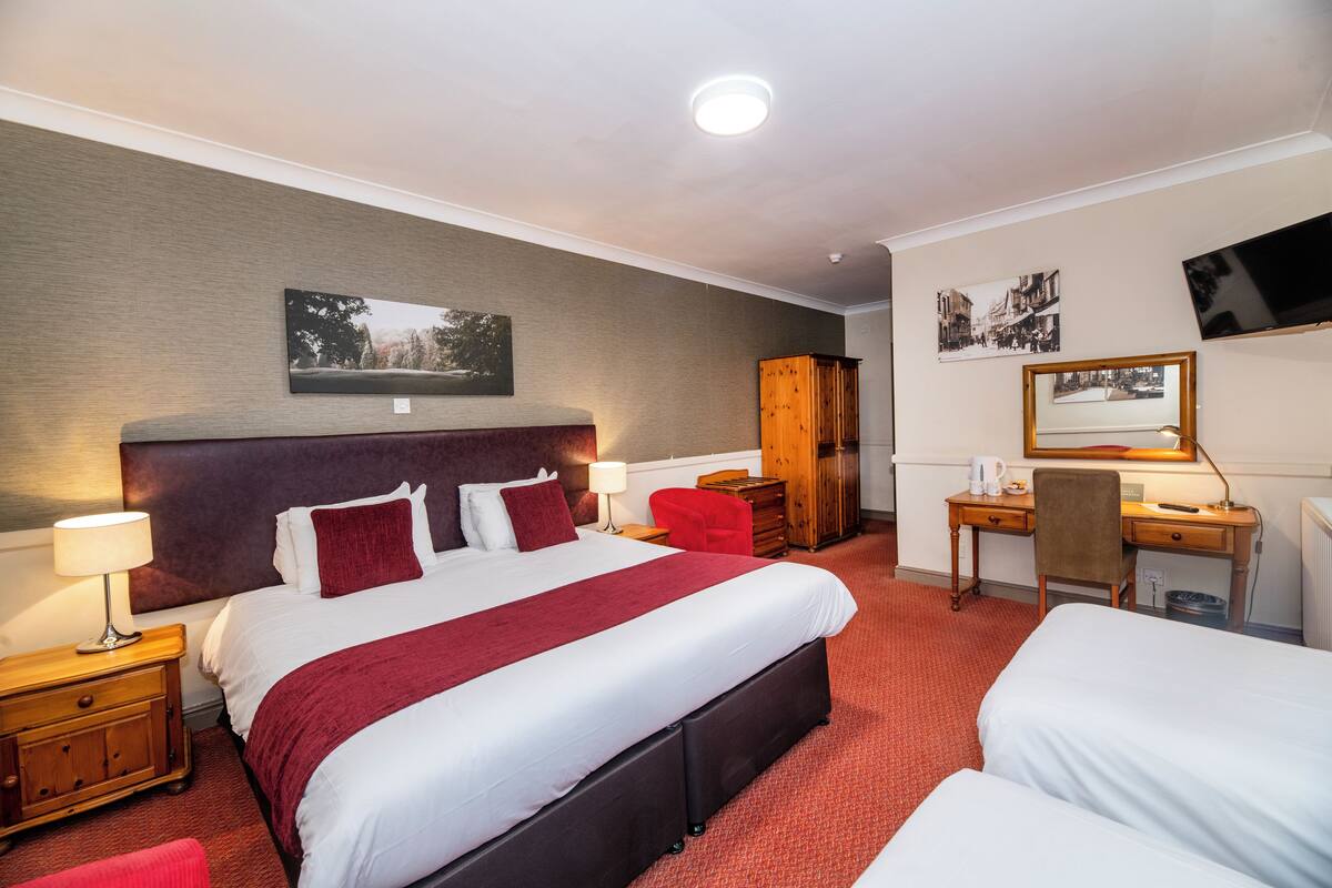 Ein Hotelzimmer mit einem großen Bett, einem Schreibtisch, einem Stuhl, einem Kleiderschrank und einem Flachbildfernseher an der Wand.