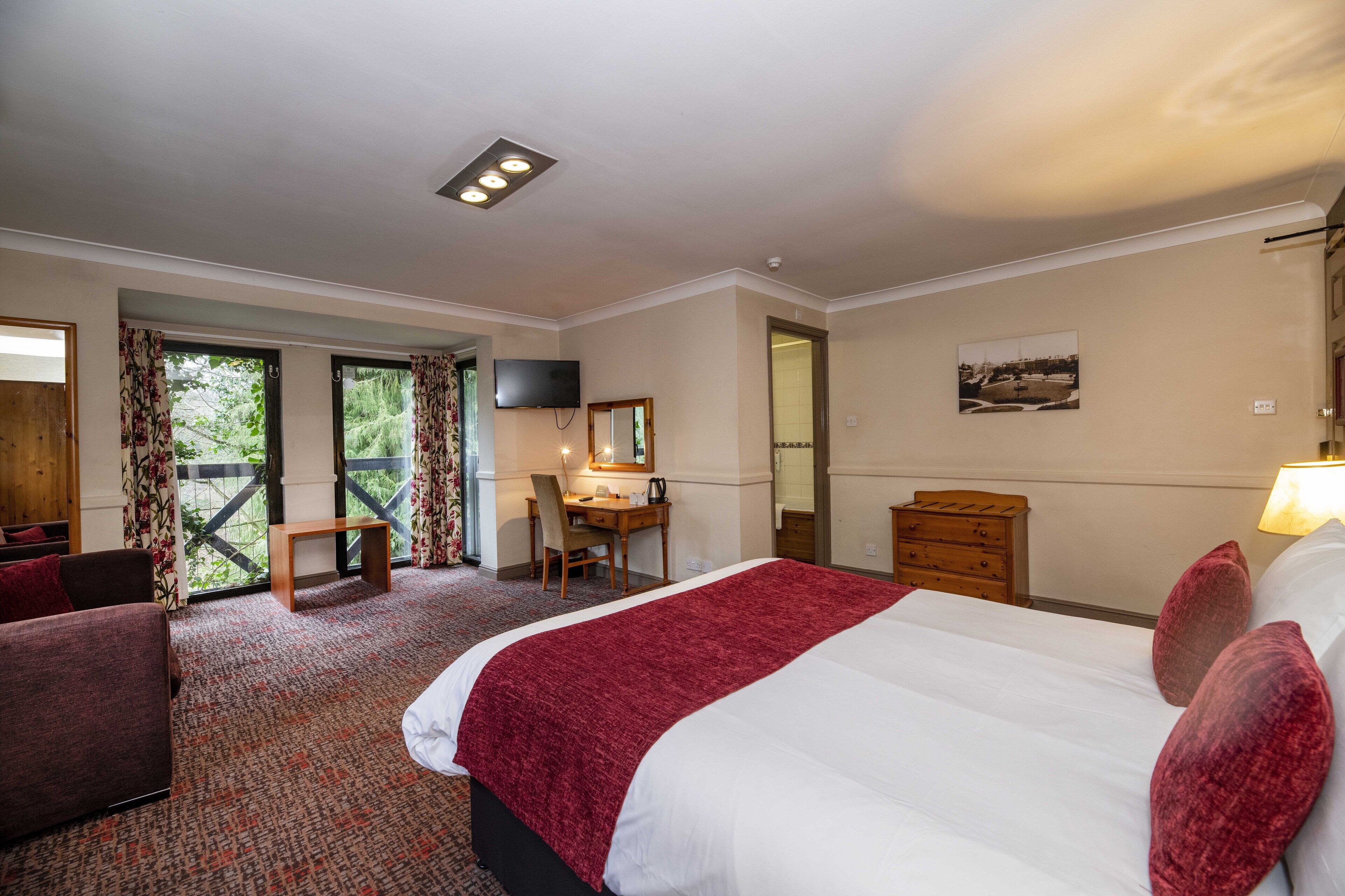 A hotel room with a large bed, a desk, a chair, a TV, and a window with curtains.