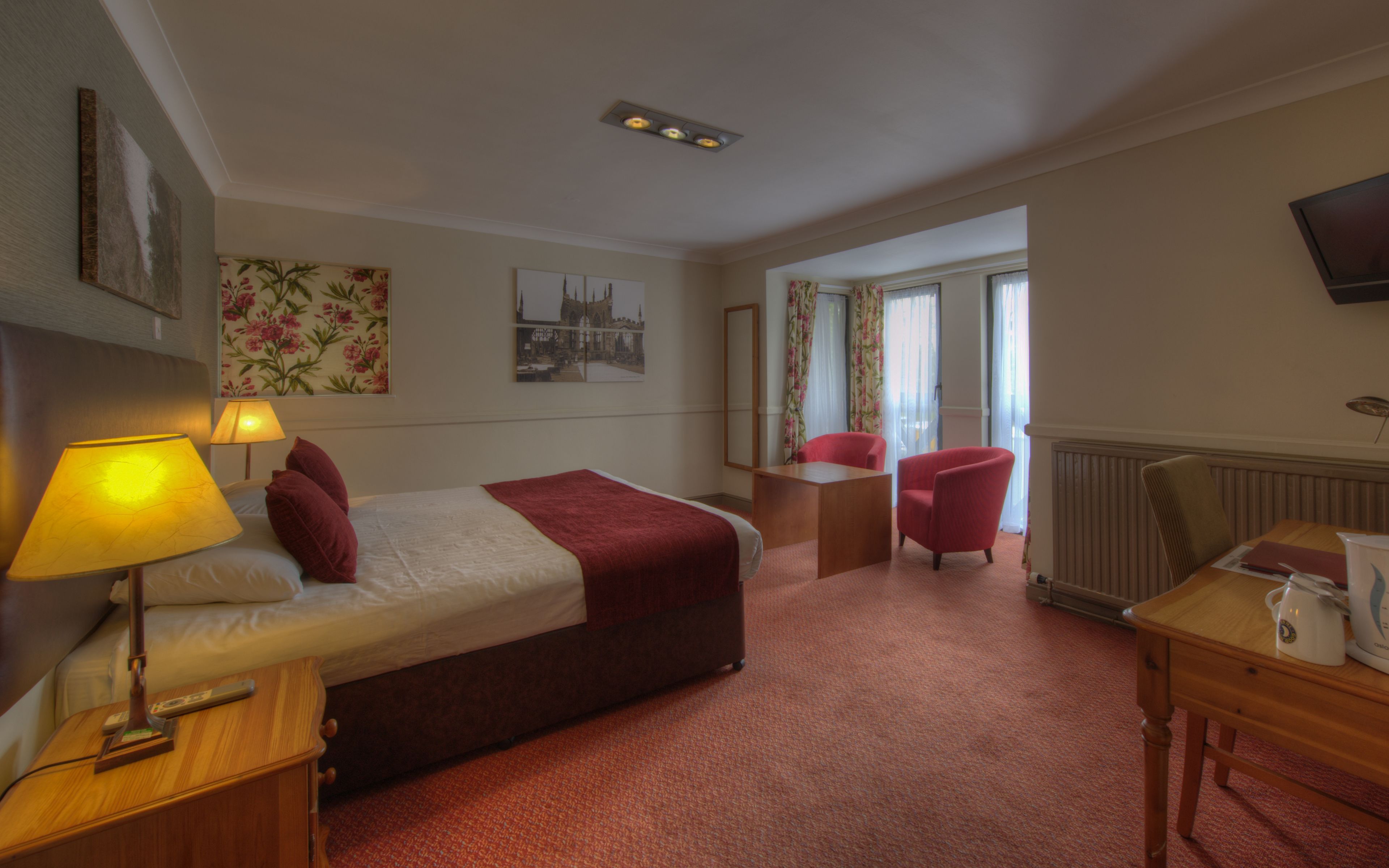 A hotel room with a bed, two bedside lamps, a desk, a chair, and a television on the wall.