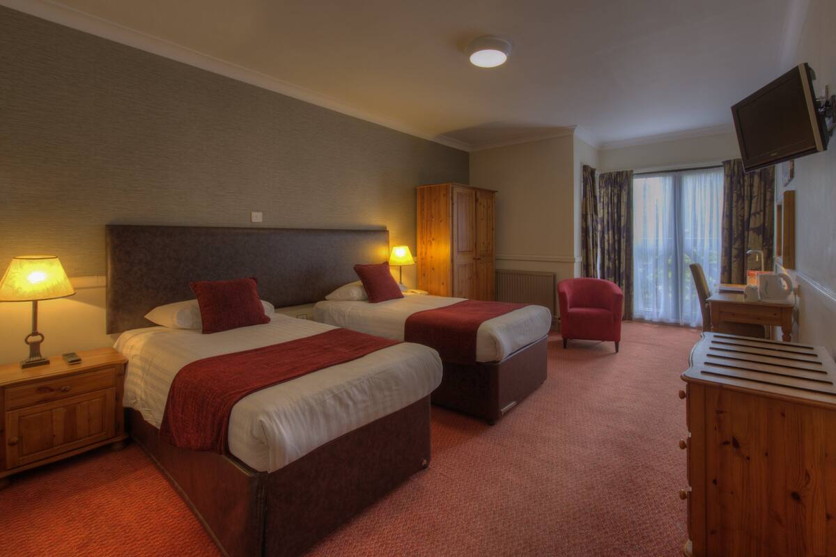 Ein Hotelzimmer mit zwei Betten, einem Holzschrank, einem Fernseher und einem Schreibtisch mit Stuhl.