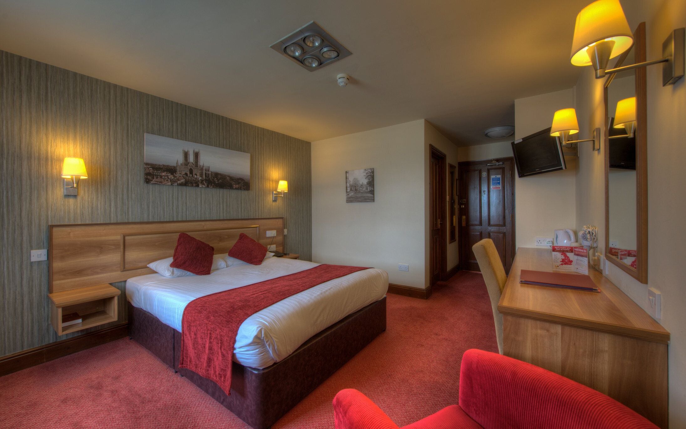 Een hotelkamer met een groot bed, een bureau, een stoel, een televisie en kunstwerken aan de wanden.