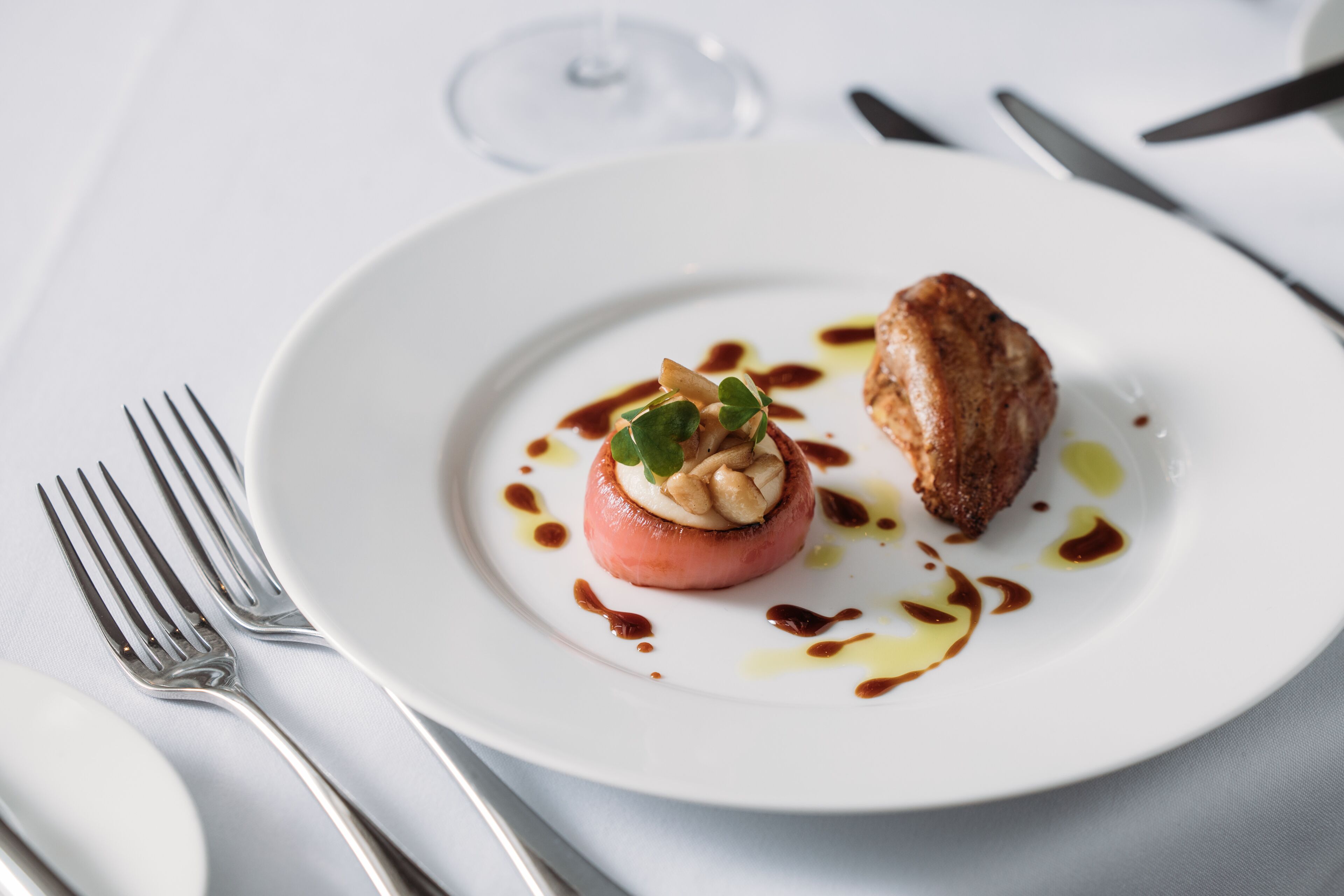 A white plate with a food item and sauce, a fork, and a knife on a white tablecloth.
