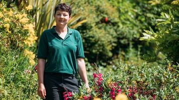 Una persona de pie en un jardín con diversas plantas y flores.