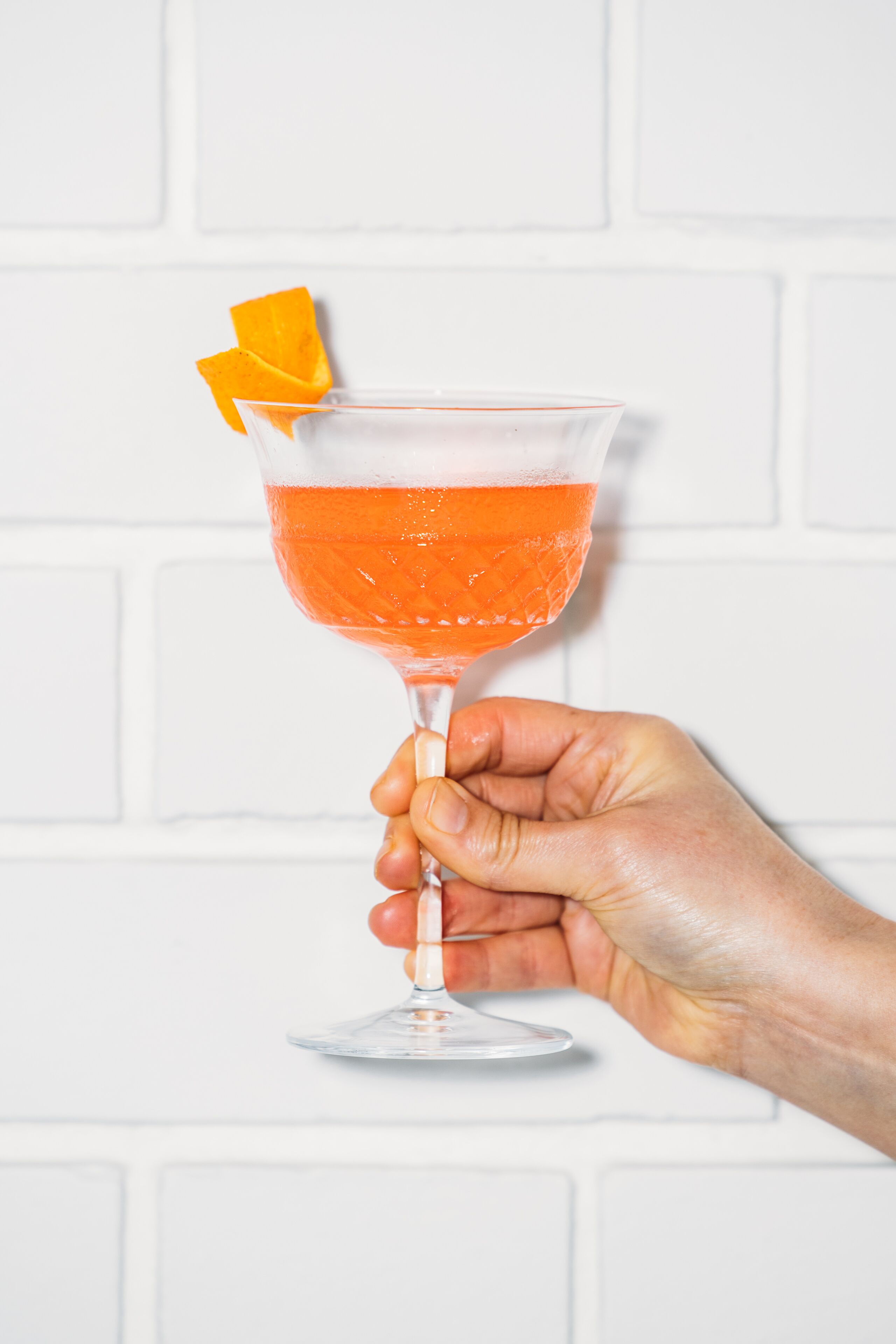 A hand holding a cocktail glass with an orange garnish.