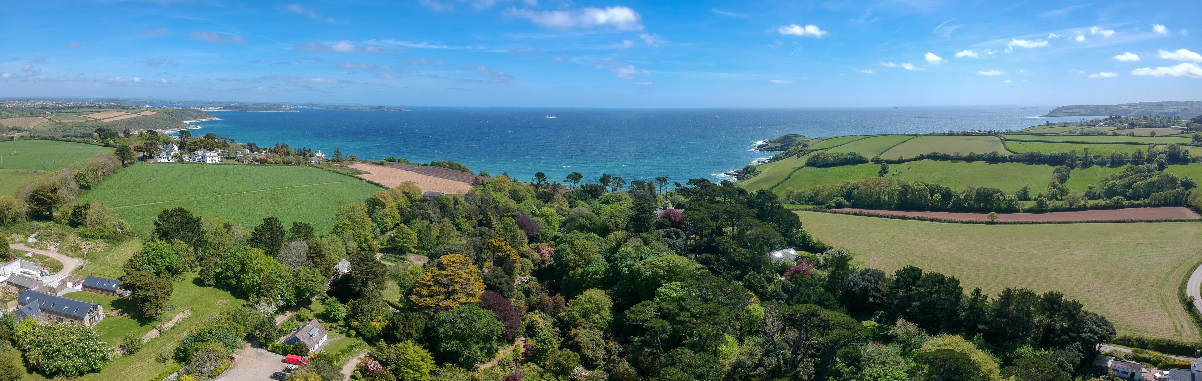 Vista aérea de una zona costera con campos verdes, árboles y una masa de agua.