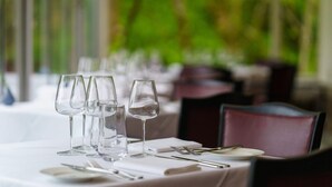 A dining table set with clear glassware, plates, and cutlery, with a view of greenery in the background. - Hotel Meudon (Falmouth)