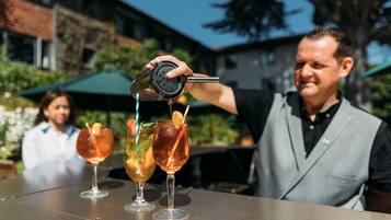 Un barman preparando bebidas en una barra al aire libre con vistas despejadas del edificio de fondo.