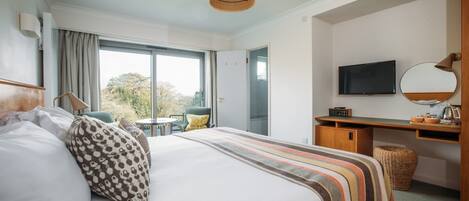 A hotel room with a large bed, a desk with a TV, a chair, and a view of the outdoors.