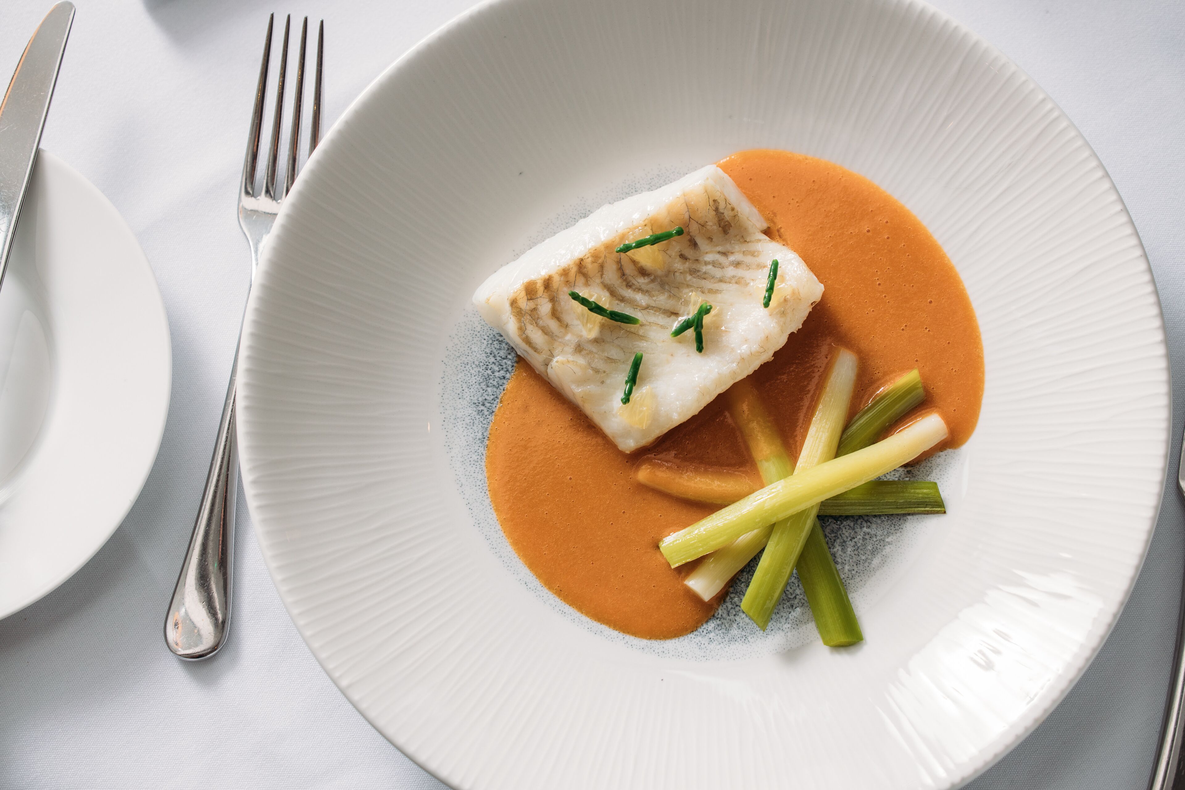 Une assiette blanche contenant un morceau de poisson, des légumes verts et une sauce.