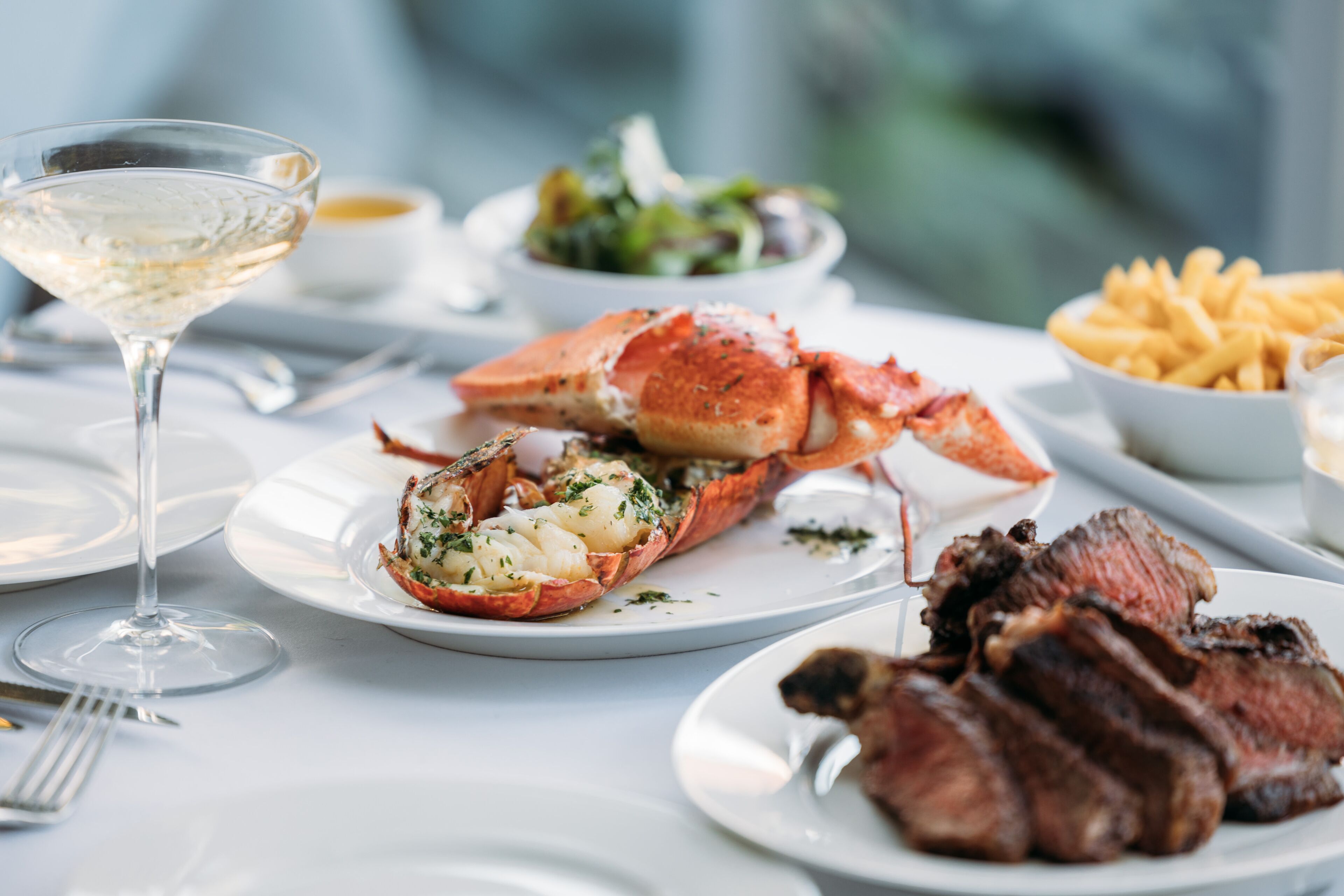 A dining table with lobster, steak, and fries.