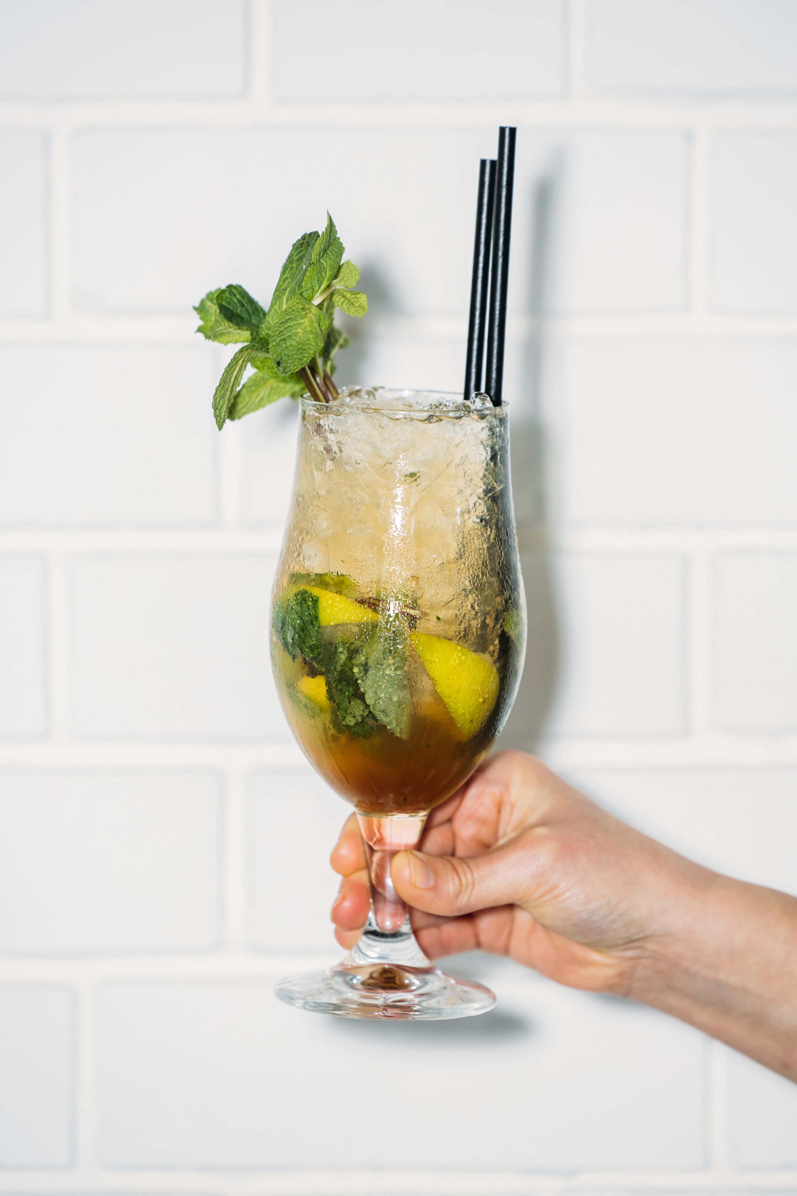 A hand holding a glass with a drink, ice, and mint leaves.