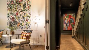Um interior moderno com piso de madeira em padrão herringbone, uma área de estar com uma poltrona e uma mesa pequena, e uma grande pintura abstrata na parede.