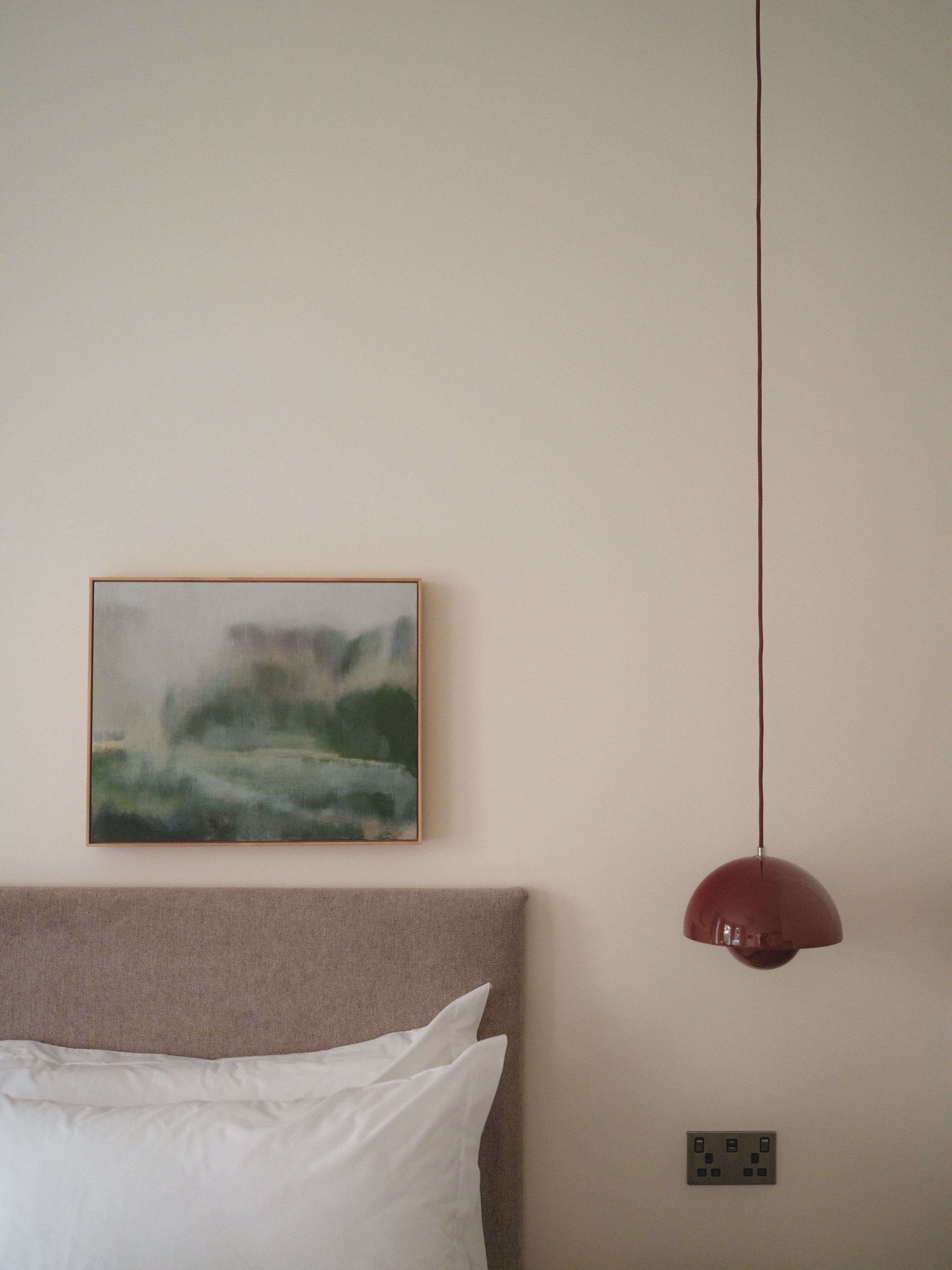A bedroom with a bed, a wall-mounted painting, a pendant light, and a power outlet.