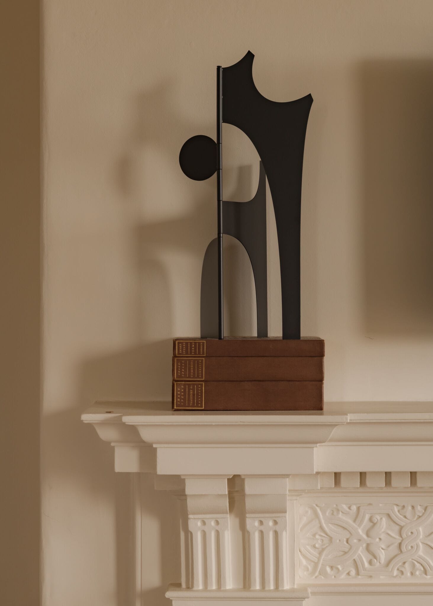 A fireplace mantel with a modern sculpture and three books.