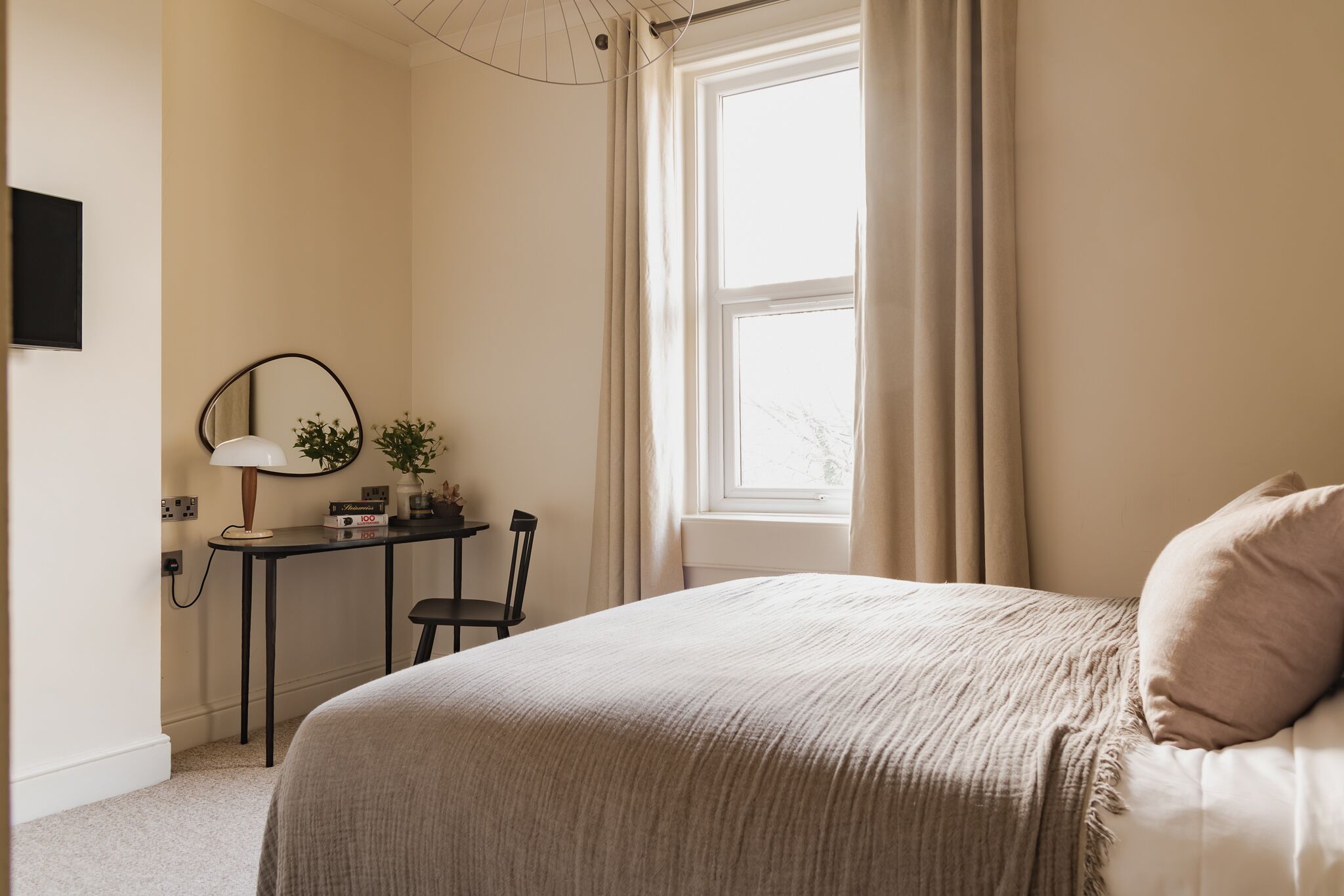 Quarto com cama, escrivaninha, cadeira, luminária e janela com cortinas.
