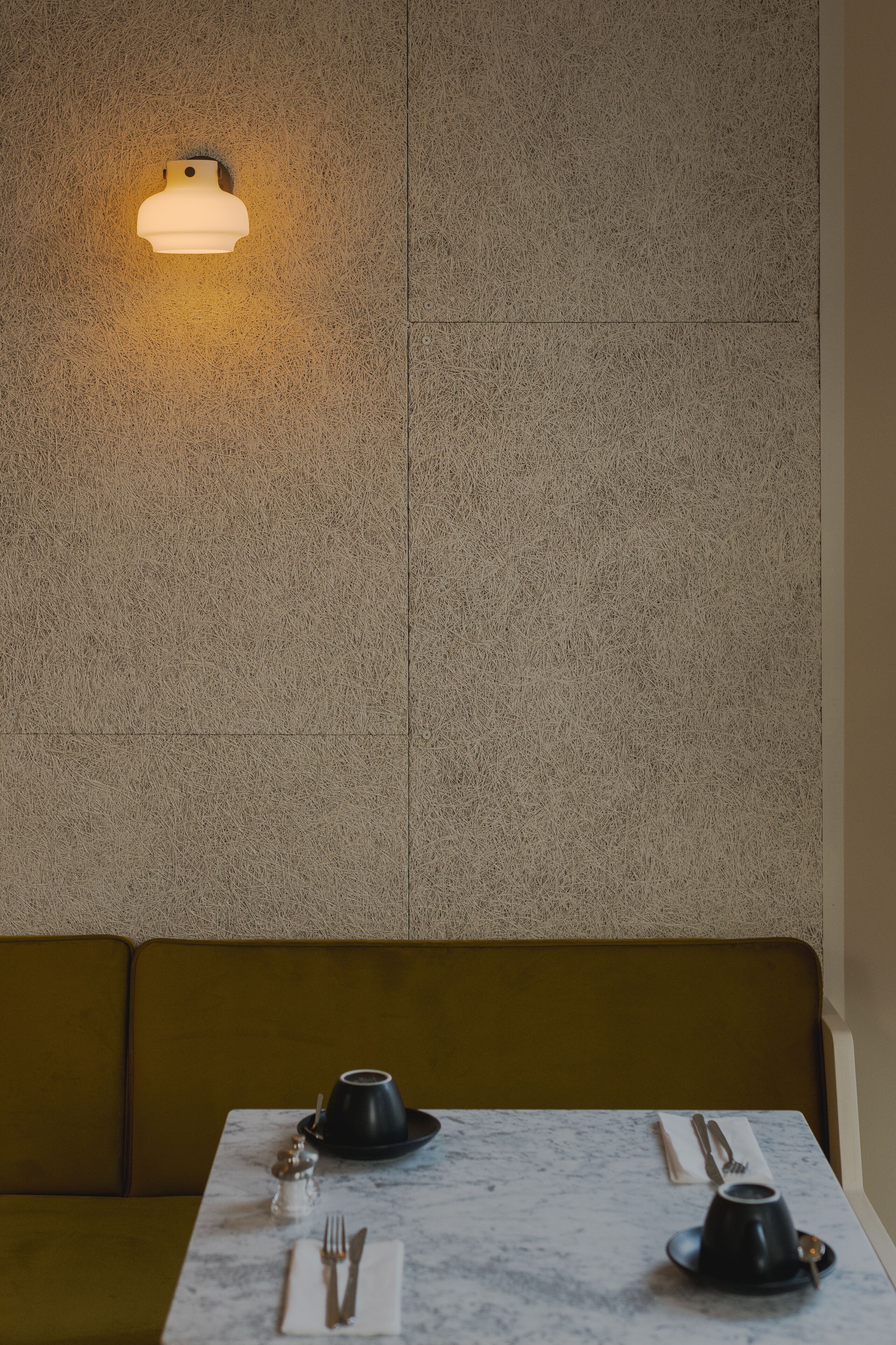 A dining area with a table set for two, a wall-mounted light fixture, and a textured wall.