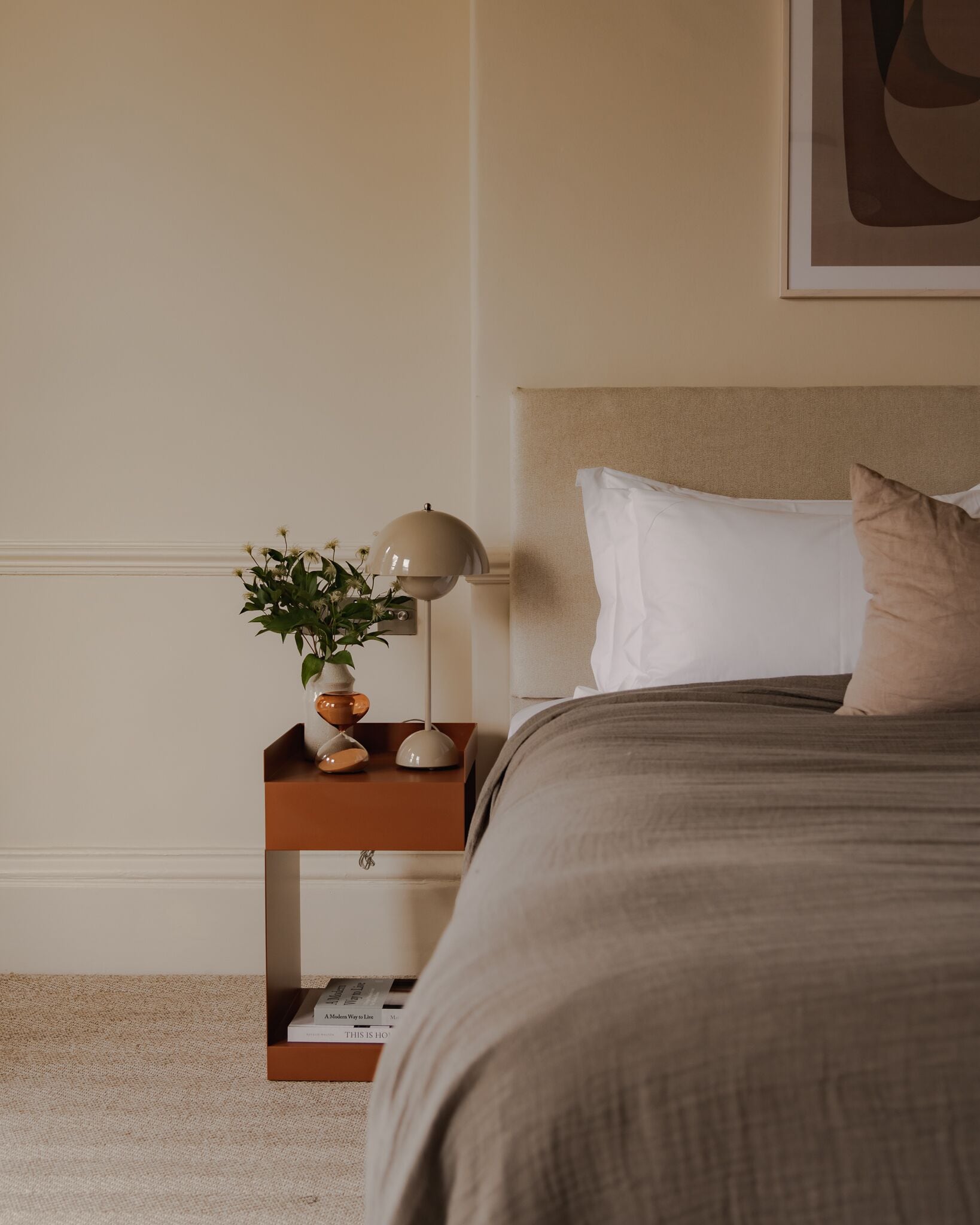 A bedroom with a bed, a nightstand, a lamp, and a plant.